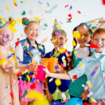 Veselá detská oslava s balónmi, tortou a deťmi hrajúcimi sa okolo stola.